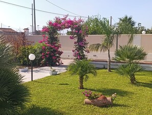 Ein gepflegter Garten mit vielfältigen Pflanzen, darunter ein markantes Blütenbogen, Palmen und ein kleines Wasserelement.