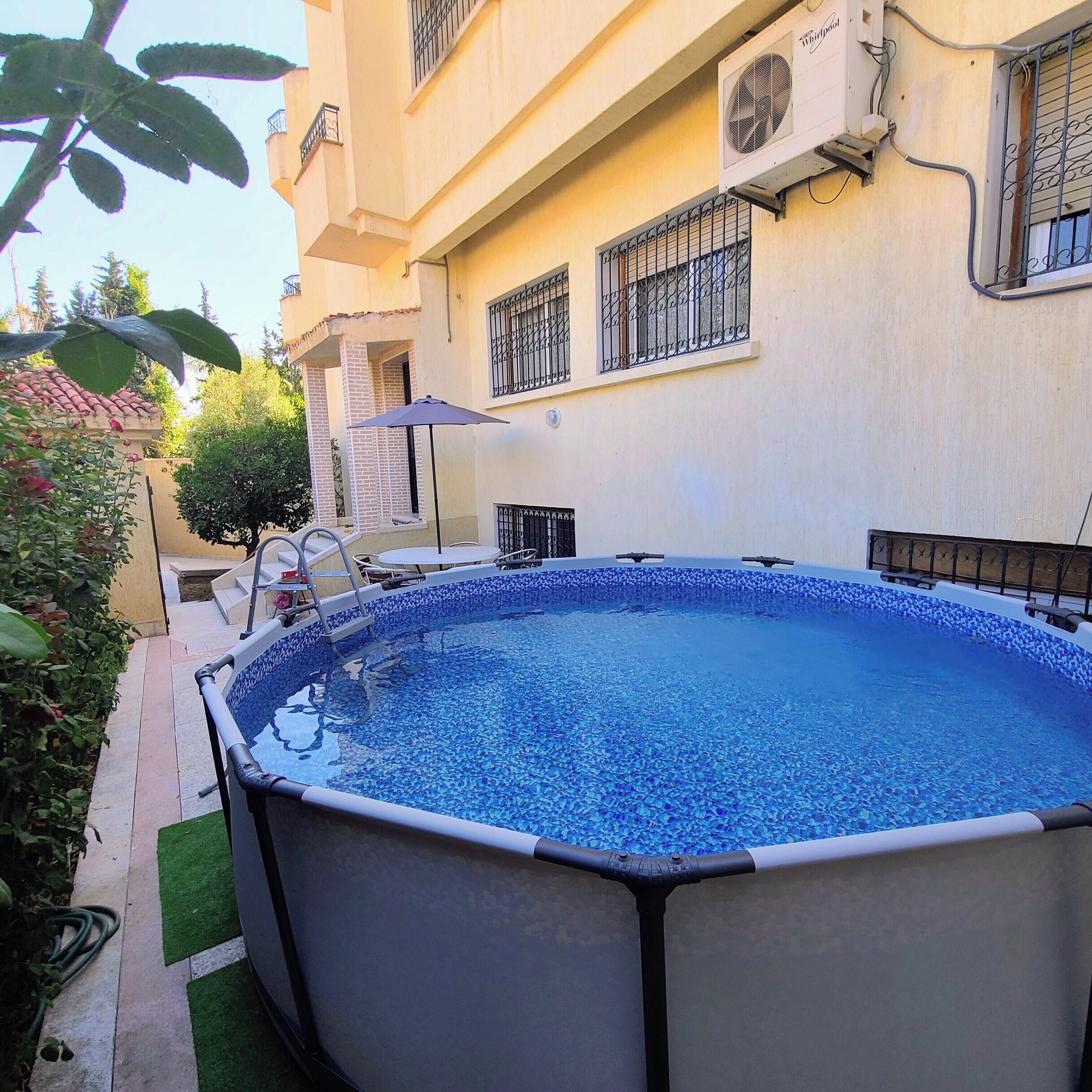 A swimming pool with a tiled edge, surrounded by a patio area with outdoor furniture.