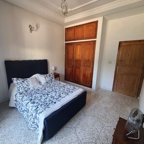 A bedroom with a large bed, wooden wardrobe, and a small bedside table.