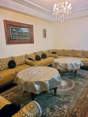 A traditional room with a sofa set, two small tables, a patterned carpet, and a chandelier.