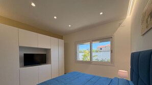 Een slaapkamer met een bed, een aan de muur bevestigde televisie, een raam met uitzicht en een lamp op het nachtkastje.