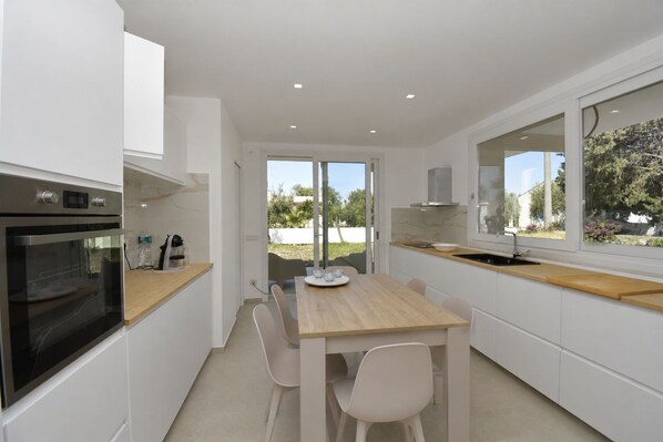 A modern kitchen with a dining area, built-in oven, and a large window offering a view of the outdoors.