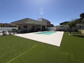 Ein modernes Haus mit Schwimmbad, einem gepflegten Rasen und blauem Himmel.
