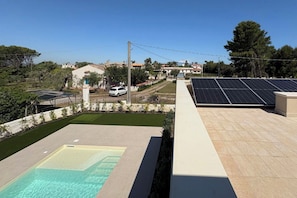A rooftop with solar panels, a swimming pool, and a view of residential buildings.