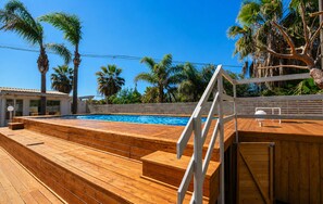 Eine Holzterrasse mit Pool, Palmen und wolkenlosem, blauem Himmel.