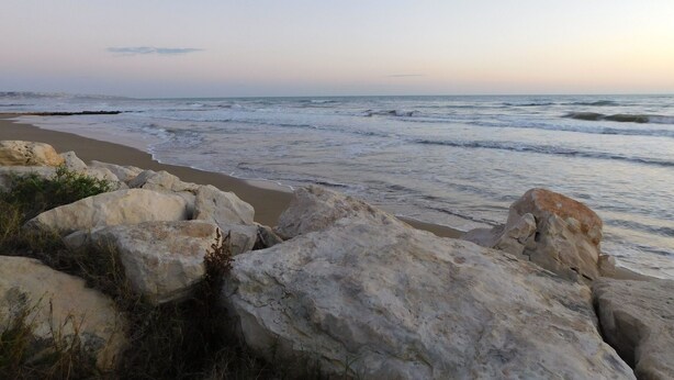 Una playa con rocas grandes al frente y olas en el fondo.