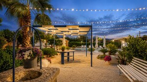 Un patio al aire libre con pérgola, asientos e iluminación colgante.