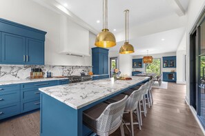 Una cocina moderna con armarios azules, encimera de mármol e isla central con taburetes de bar.