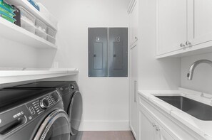 A compact laundry room with a front-loading washing machine, a sink, and two doors labeled 'C' and 'D'. - Brand new build in new Ocean Park area (Kiawah Island)