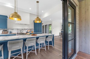 A modern kitchen with a marble countertop, blue cabinets, and white wicker bar stools. - Brand new build in new Ocean Park area (Kiawah Island)
