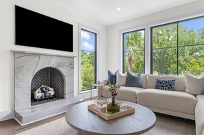 A modern living room with a fireplace, a large window, and a sofa. - Brand new build in new Ocean Park area (Kiawah Island)