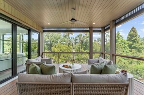 Ein geräumiger Balkon mit Rattan-Sofa, einem runden Tisch und einer Snackplatte sowie einem Deckenventilator.