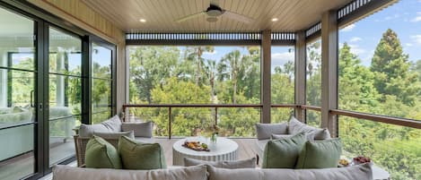 A spacious balcony with a wicker sofa, a round table with a tray of snacks, and a ceiling fan.
