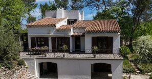 Un bâtiment à deux étages, doté d’un toit en tuiles, de nombreuses fenêtres avec volets et d’un balcon orné de plantes en pot.