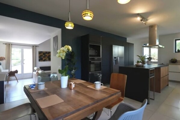 Une cuisine moderne dotée d’un îlot central, d’appareils électroménagers intégrés et de luminaires suspendus.