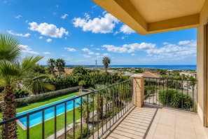 A balcony with a view of a swimming pool, palm trees, and a distant coastline. - Beautiful private villa with A/C, WIFI, private pool, TV, veranda, pets allowed and panoramic view (Donnalucata)