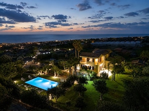 Ein Wohnhaus mit Swimmingpool, üppigem Grün und Blick auf das Meer im Abendlicht.