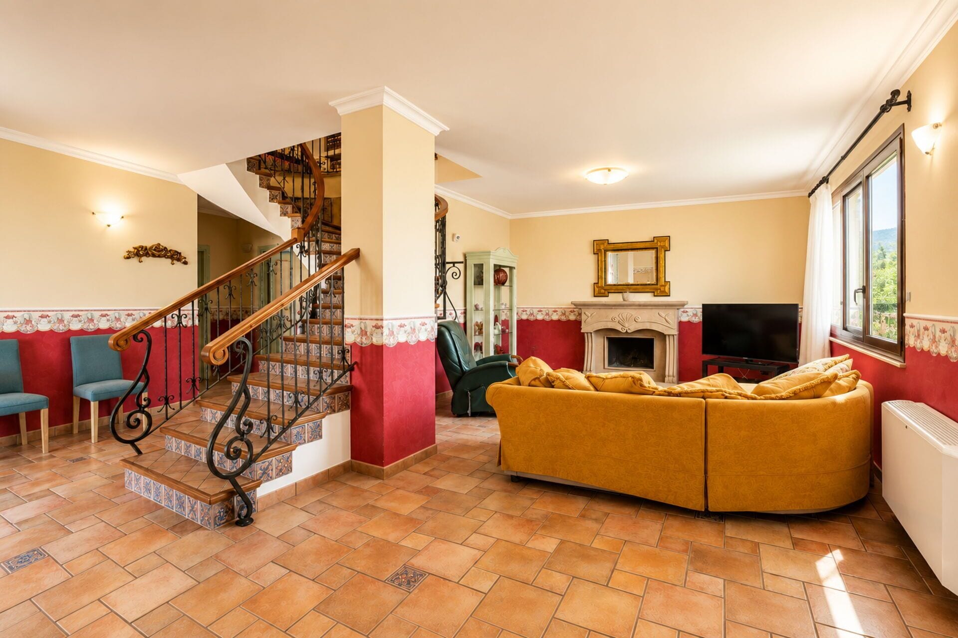 A living room with a curved sofa, a fireplace, a television, and a staircase with decorative railings.