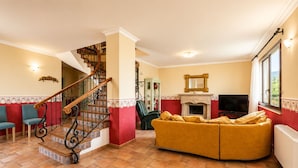 Una sala de estar con un sofá curvo, una chimenea, un televisor y una escalera con barandilla decorativa.
