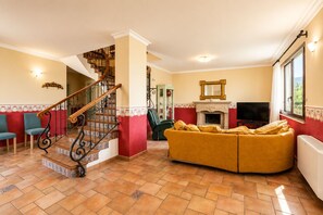 Ein Wohnzimmer mit einer gebogenen Couch, einem Kamin, einem Fernseher und einer Treppe mit dekorativer Geländer.