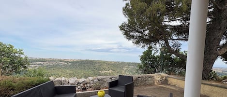 Espaço ao ar livre com mobiliário de vime e parede de pedra, com vista para uma paisagem ondulada.