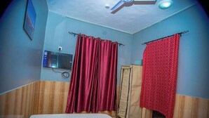 A room with a bed, a red curtain, a wooden wall, and a ceiling fan. - LE MIA KD LODGE (Sekondi-Takoradi)
