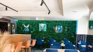 A restaurant interior with blue upholstered chairs, wooden tables, a green wall with artwork, and a modern ceiling design. - THE 8 HOTEL BUDAPEST (Budapest)