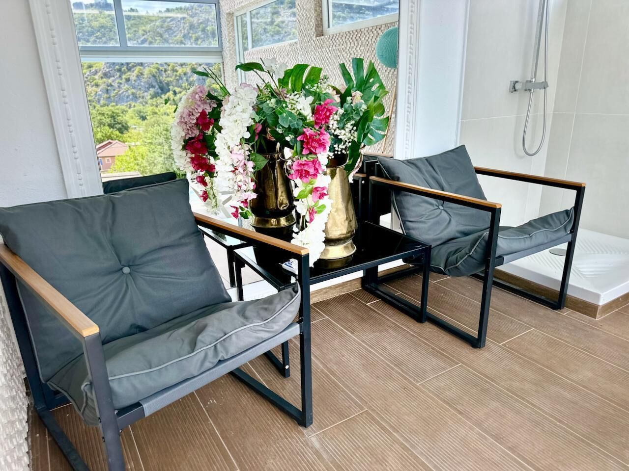 A balcony with two grey cushioned chairs, a small table, and a floral arrangement.