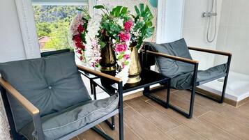 A balcony with two grey cushioned chairs, a small table, and a floral arrangement.
