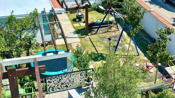 Un parque infantil con diversas estructuras de juego, una zona de estar cubierta y un pequeño jardín con plantas en macetas.