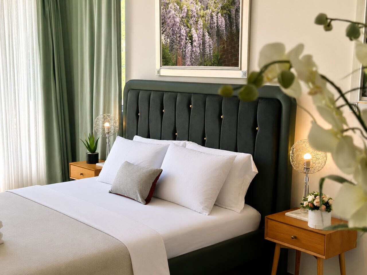 A neatly made bed with white linens and a dark headboard, a bedside table with a lamp, and a framed picture on the wall.