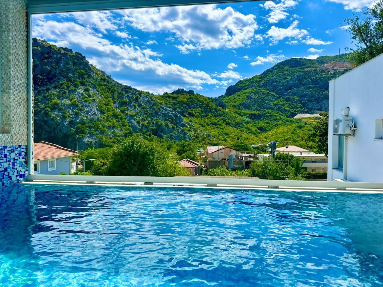 A swimming pool with clear blue water, surrounded by lush green hills and a partly cloudy sky.
