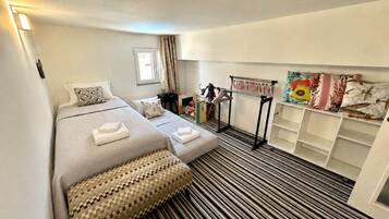 A hotel room with a bed, a bedside table, a lamp, a window with curtains, and a storage unit with shelves.