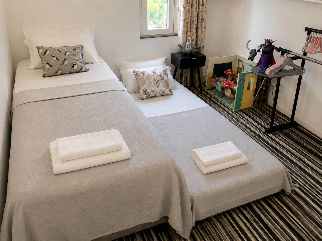 A hotel room with two beds, a small table, a chair, and a window with curtains.