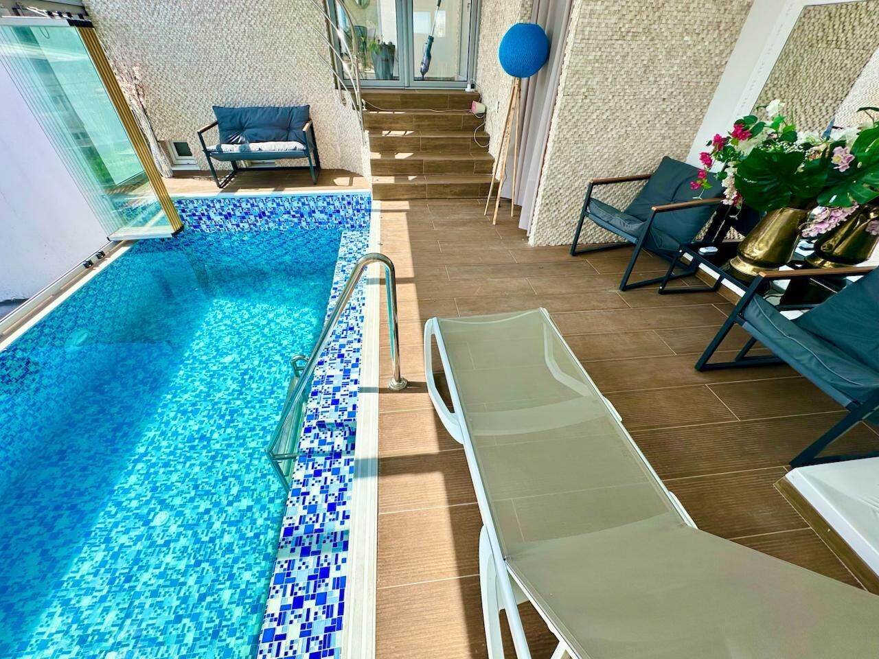An indoor swimming pool with a tiled edge, a sun lounger, and a staircase leading to an upper level.