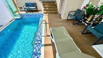 An indoor swimming pool with a tiled edge, a sun lounger, and a staircase leading to an upper level.