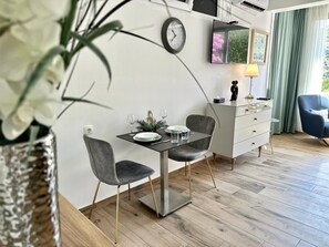 A modern dining area with a table set for two, a clock on the wall, and a sofa in the background.