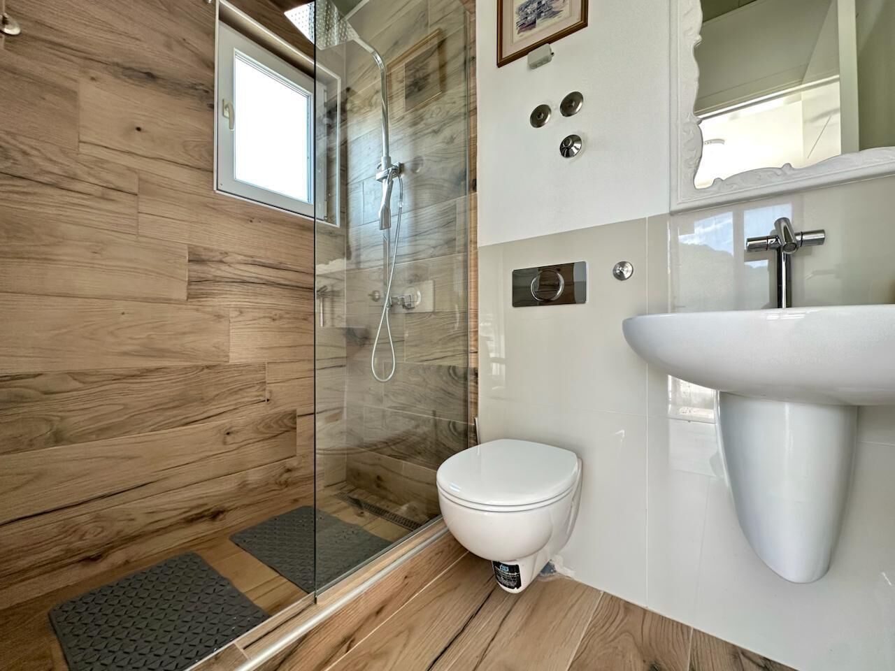 Un baño moderno con cabina de ducha de vidrio, inodoro blanco y lavamanos pedestal.