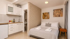 Una habitación de hotel moderna con una cama, una mesita de noche pequeña, un cuadro colgado en la pared con un león y una zona de cocina con armarios y encimera.