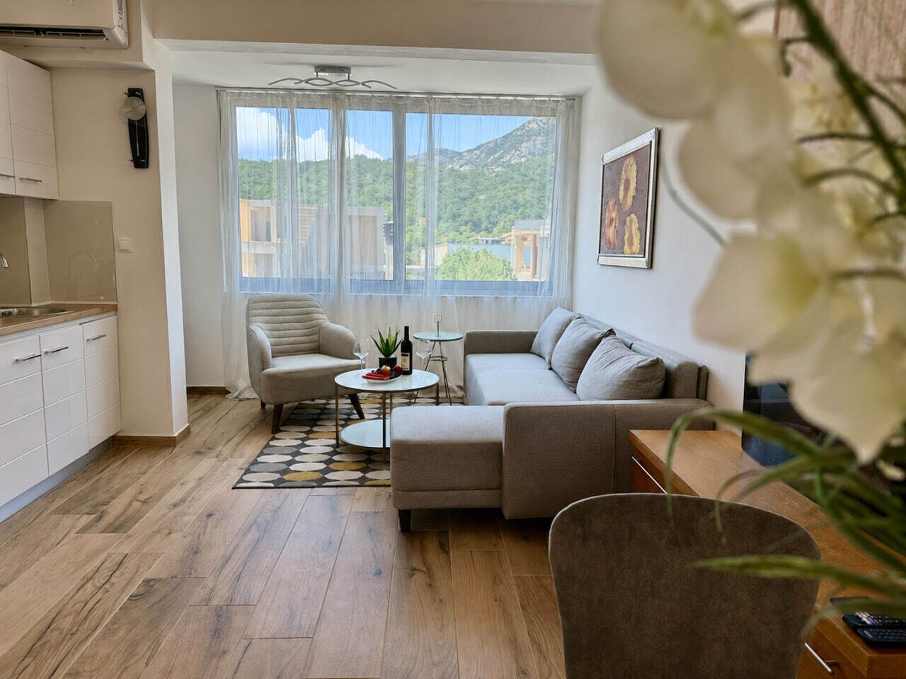 A living room with a sofa, a chair, a small table, and a view of a mountain through a window.
