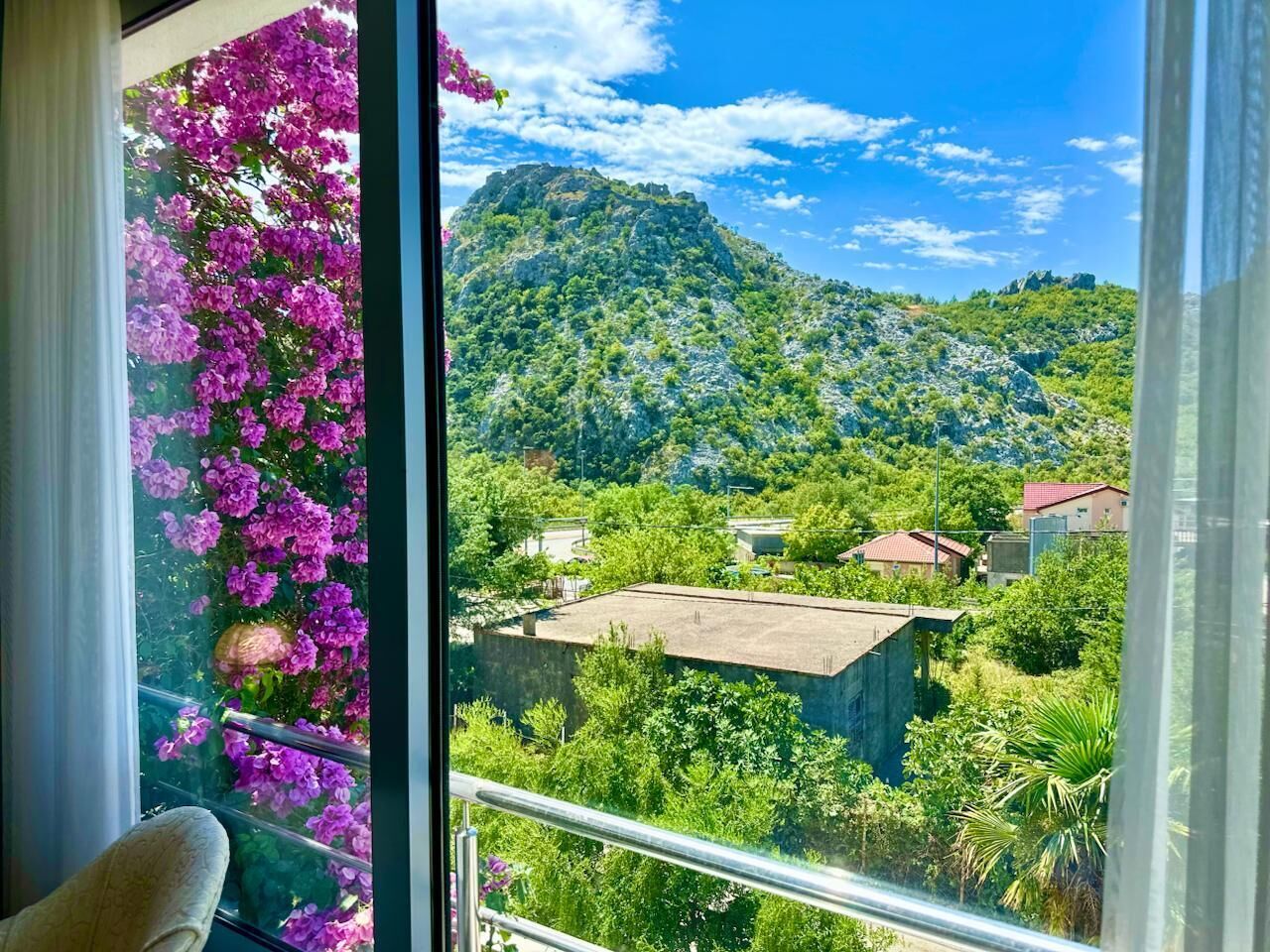 A balcony with a view of a mountainous landscape, a building with a flat roof, and a chair.