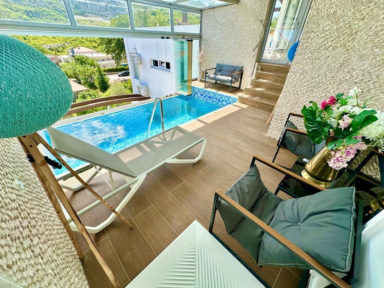 Un área de piscina interior moderna con balaustrada de vidrio, sillas de descanso y vistas al paisaje circundante.