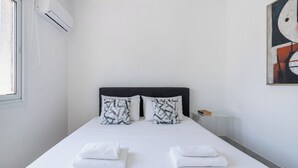 Ett hotellrum med en säng, två kuddar, ett nattduksbord, en lampa och en tavla på väggen.