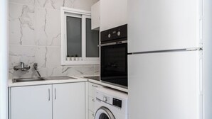 Ett kompakt kök med en inbyggd ugn, en tvättmaskin och ett fönster ovanför diskbänken.