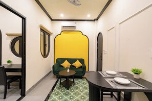 A compact living space with a dining area, a sofa with yellow cushions, and a small table with a vase. - NHA TRONG NGO 2 (Da Nang)