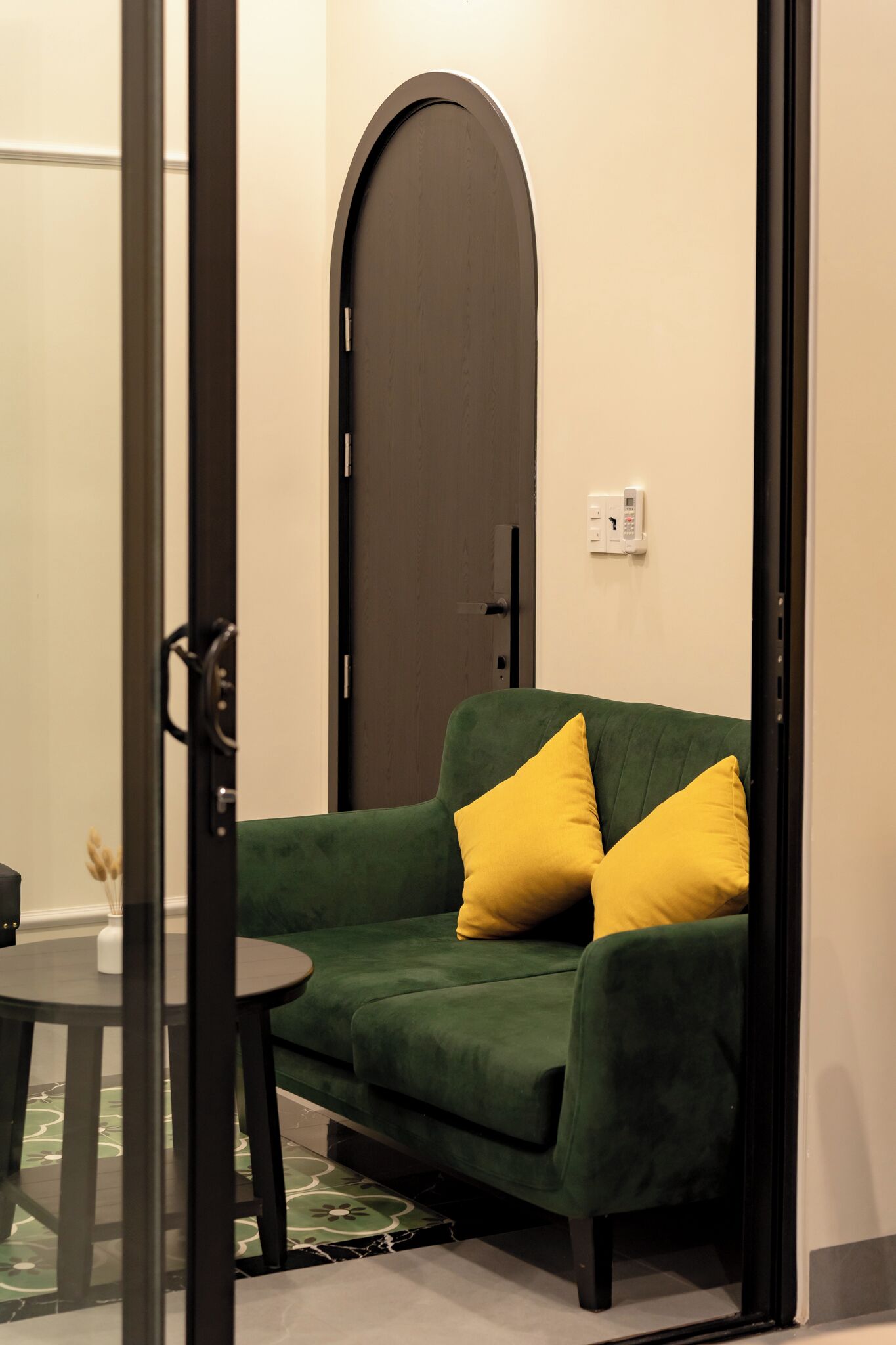 A green sofa with yellow cushions, a small round table, and a door with a keypad lock.