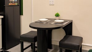 A compact room with a black refrigerator, a small table with two stools, and a potted plant. - NHA TRONG NGO 2 (Da Nang)