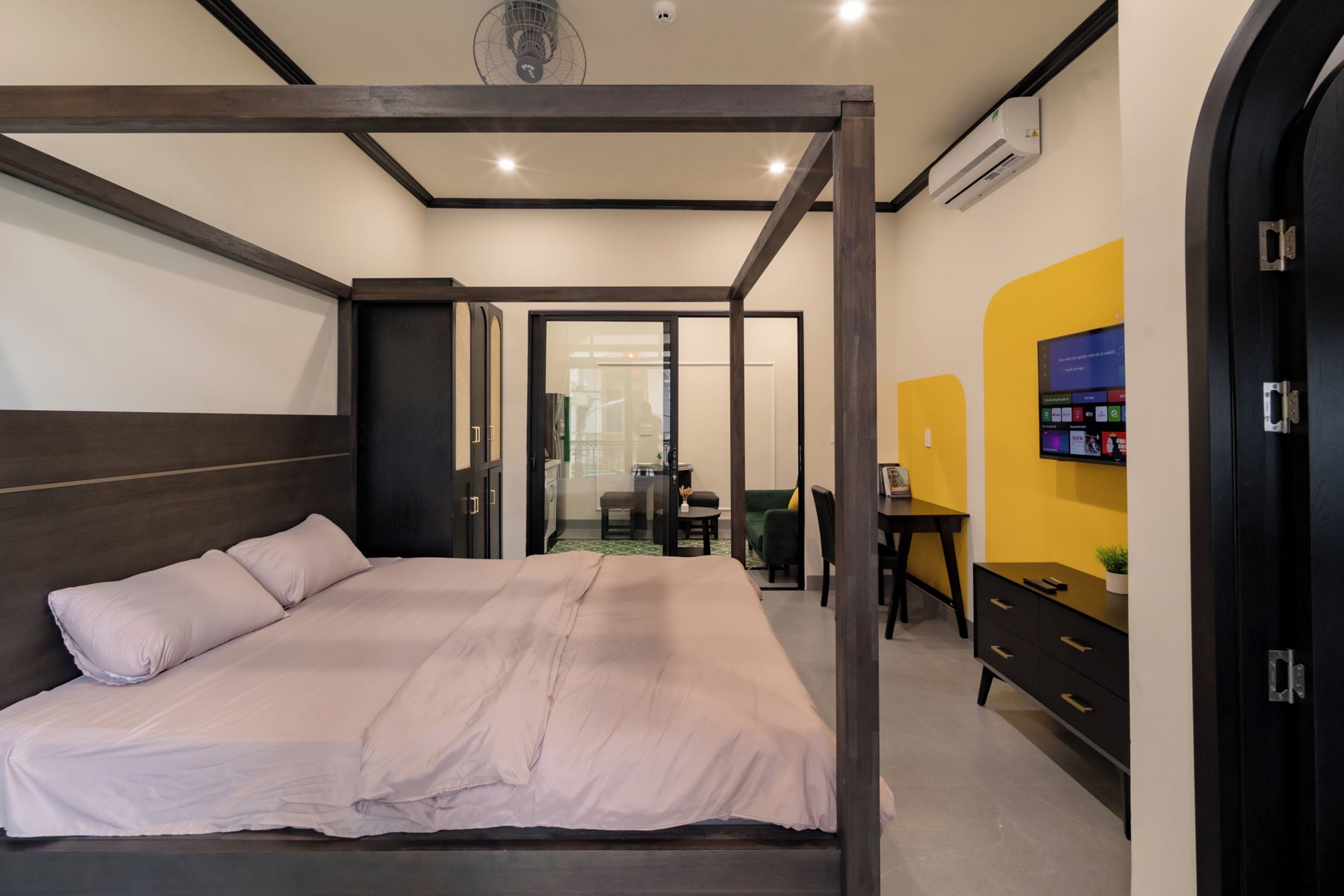 Un dormitorio moderno con cama con dosel, escritorio y televisor en la pared.