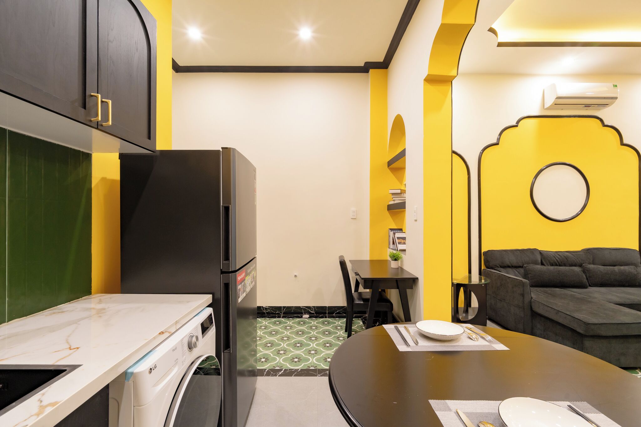 A compact kitchen with a refrigerator, a dining table set for two, and a sofa in a living area.