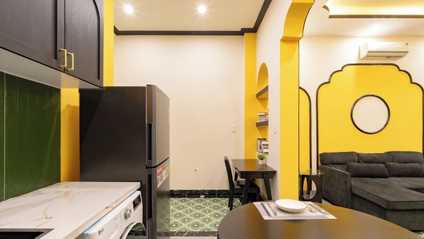 A compact kitchen with a refrigerator, a dining table set for two, and a sofa in a living area. - NHA TRONG NGO 2 (Da Nang)